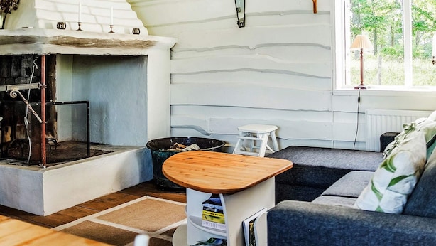 Una sala de estar acogedora con chimenea, un sofá, una mesita y un ventanal con vistas al verdor.