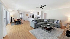 Uma sala de estar moderna com um sofá cinzento, uma mesa de centro e uma área de refeições com uma mesa e cadeiras.