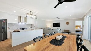 Cozinha moderna com armários brancos, uma ilha central e uma área de refeições com mesa e cadeiras de madeira.