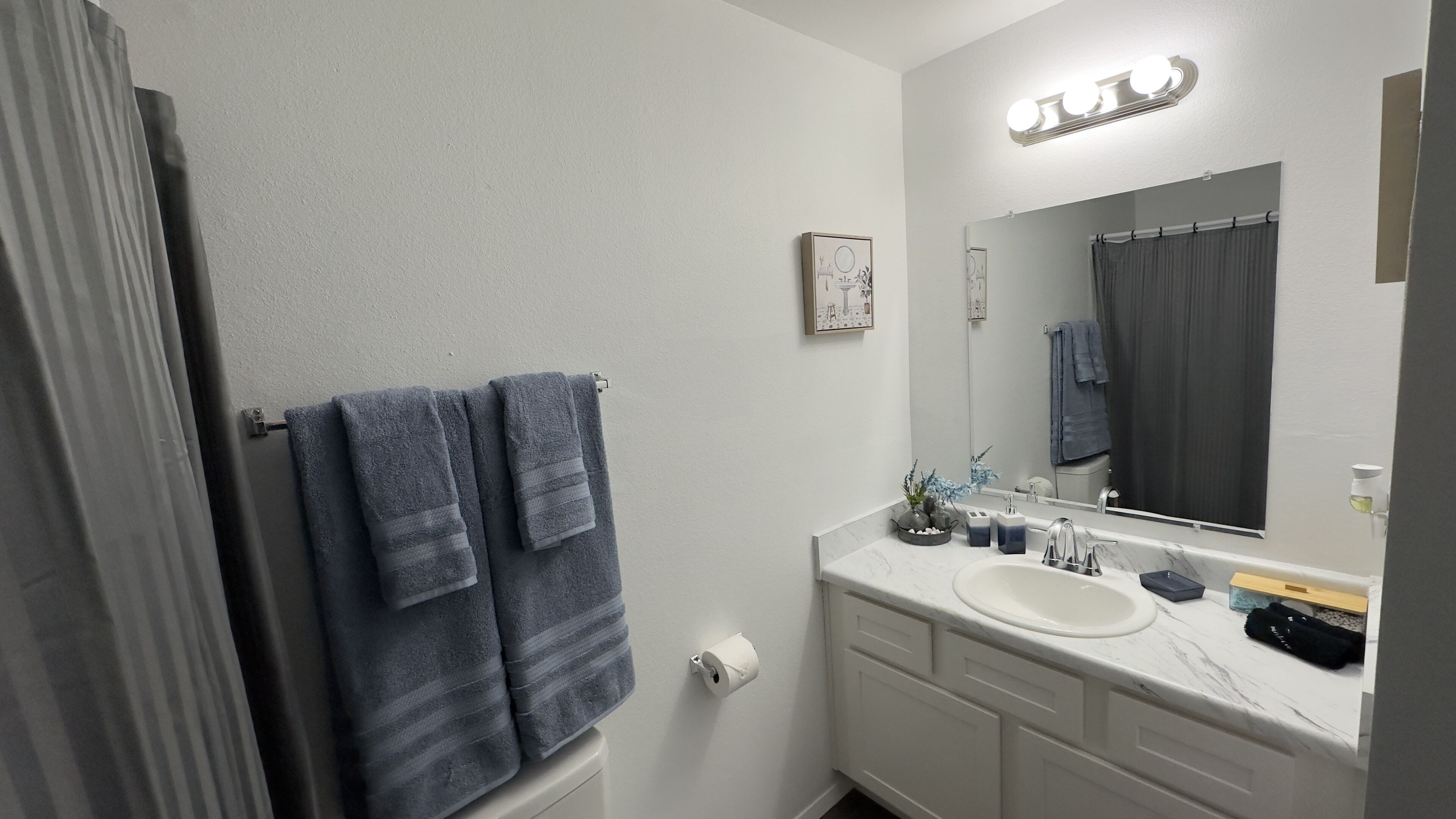 Un bagno con un mobile lavabo bianco, un grande specchio e un porta asciugamani con tre asciugamani.