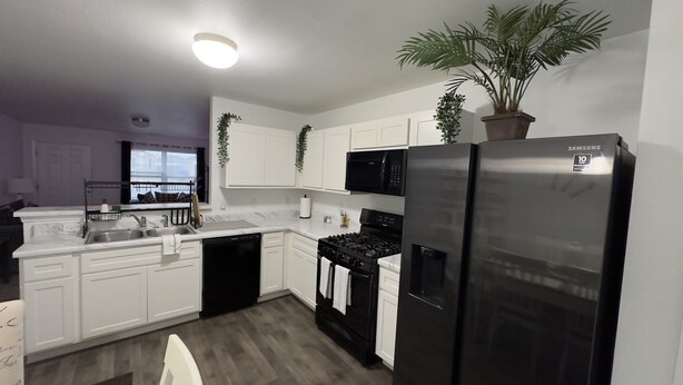 A modern kitchen with white cabinets, a black refrigerator, a stove, and a microwave. - Welcome to Innovators Home Broken Arrow with Large Driveway (Broken Arrow)