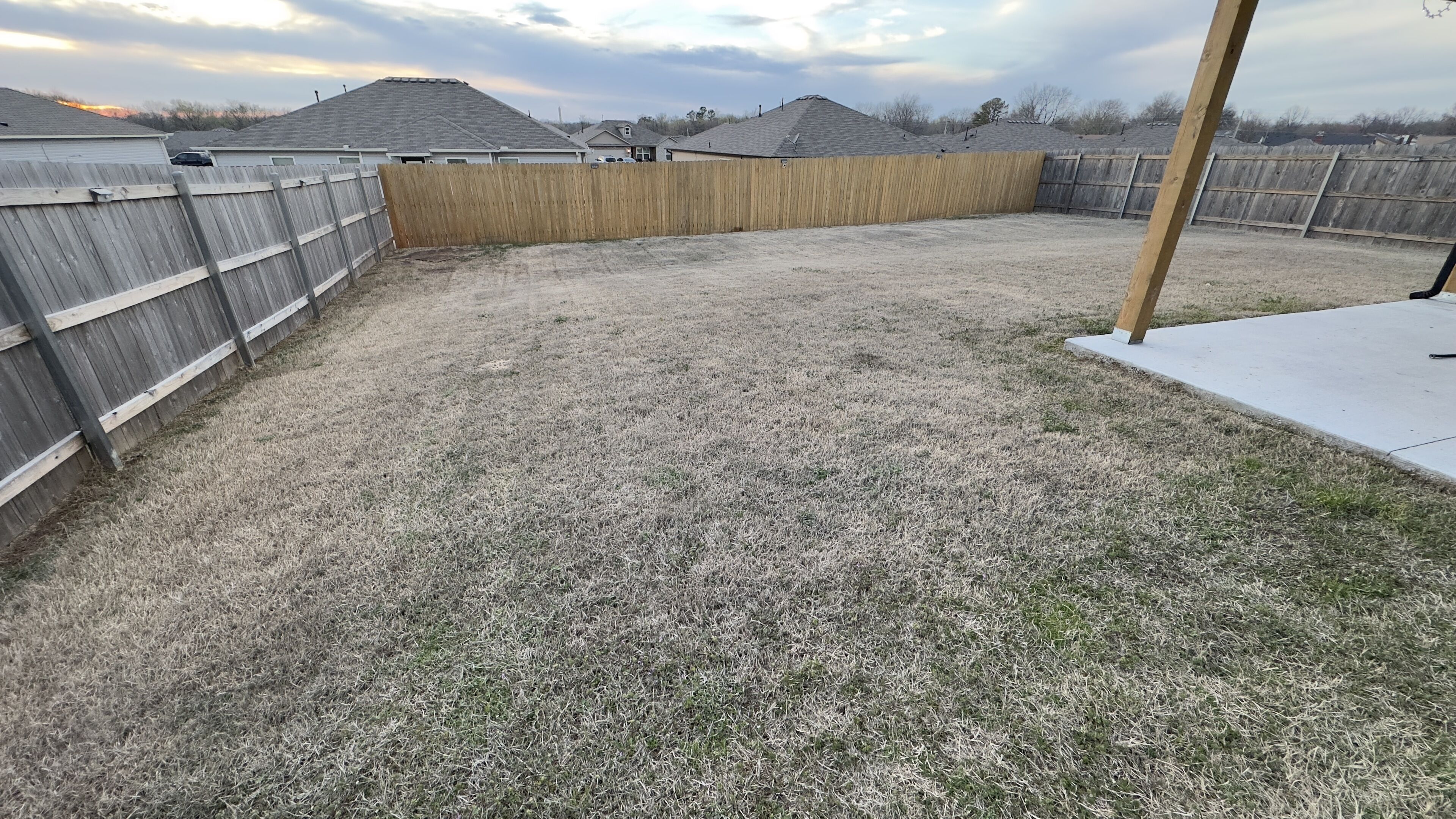 A backyard with a wooden fence, a concrete patio, and a grassy area.