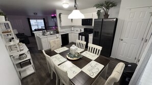 A modern kitchen with white cabinets, a black refrigerator, and a dining table set with placemats. - Welcome to Innovators Home Broken Arrow with Large Driveway (Broken Arrow)