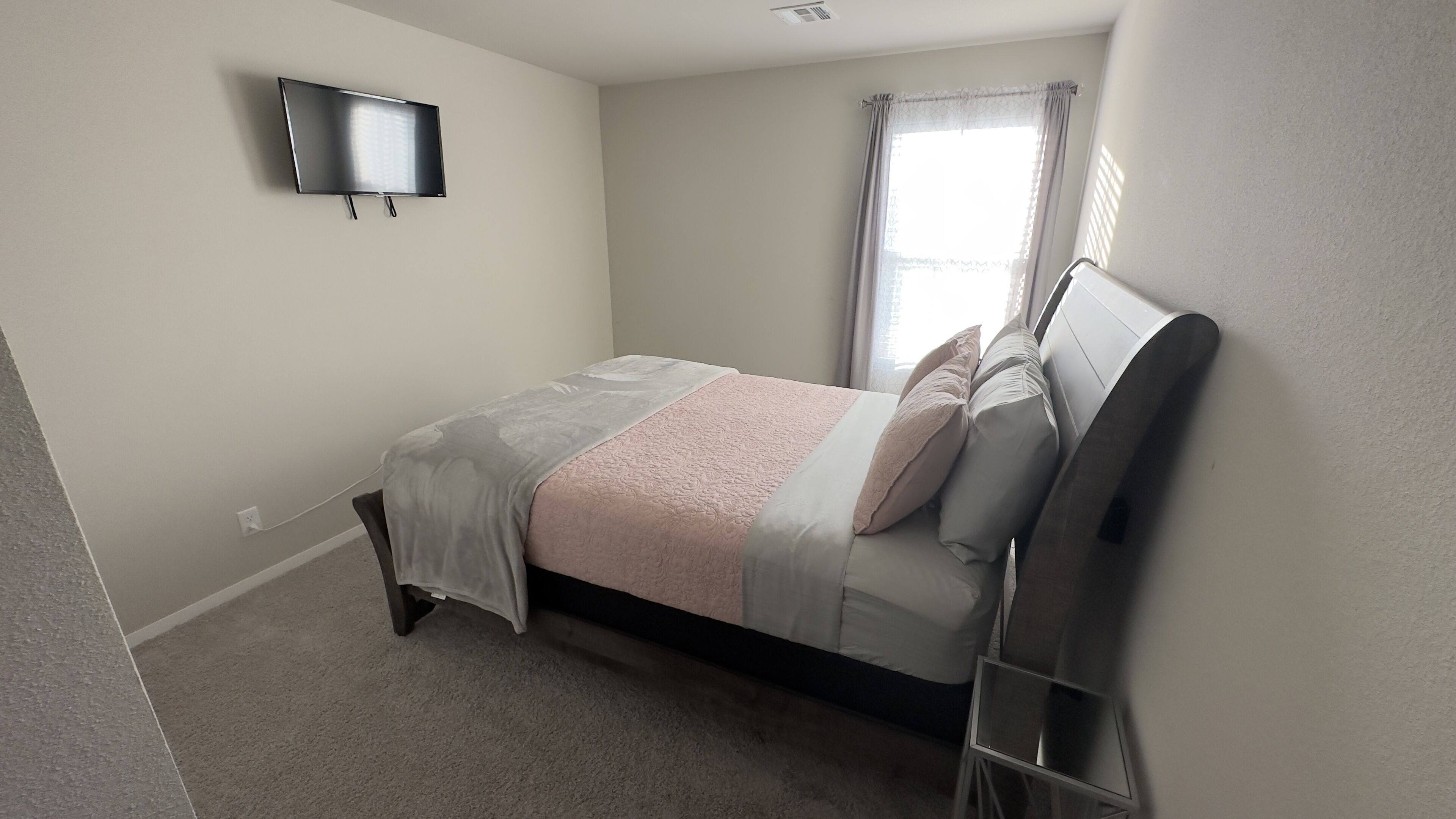 Un dormitorio con cama, televisión montada en la pared y ventana con cortinas.