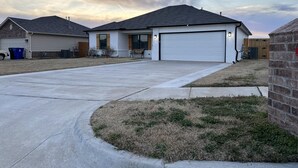 A residential area with houses, a driveway, and a grassy lawn. - Welcome to Innovators Home Broken Arrow with Large Driveway (Broken Arrow)