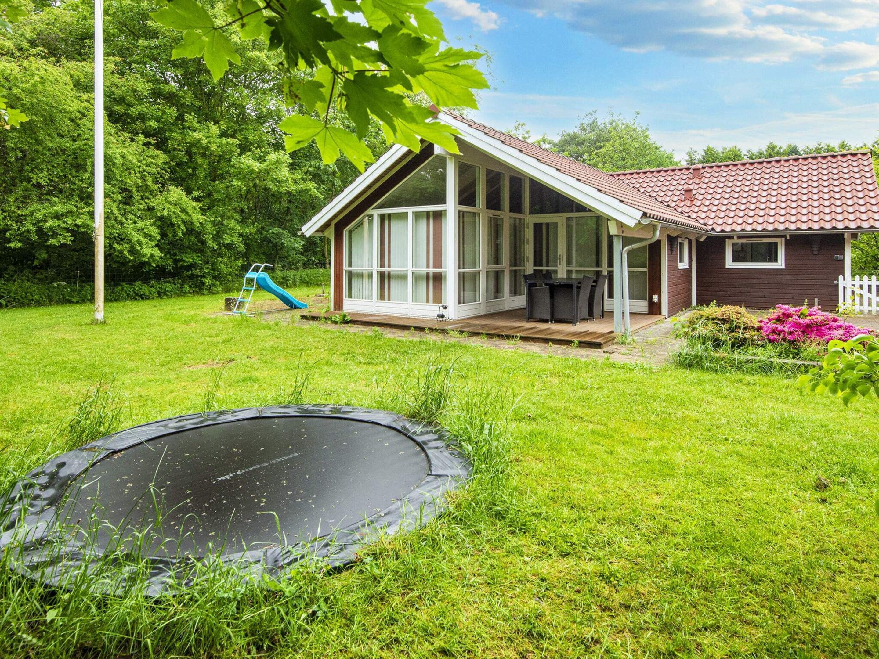 A house with a covered patio, a trampoline, and a slide in the yard.