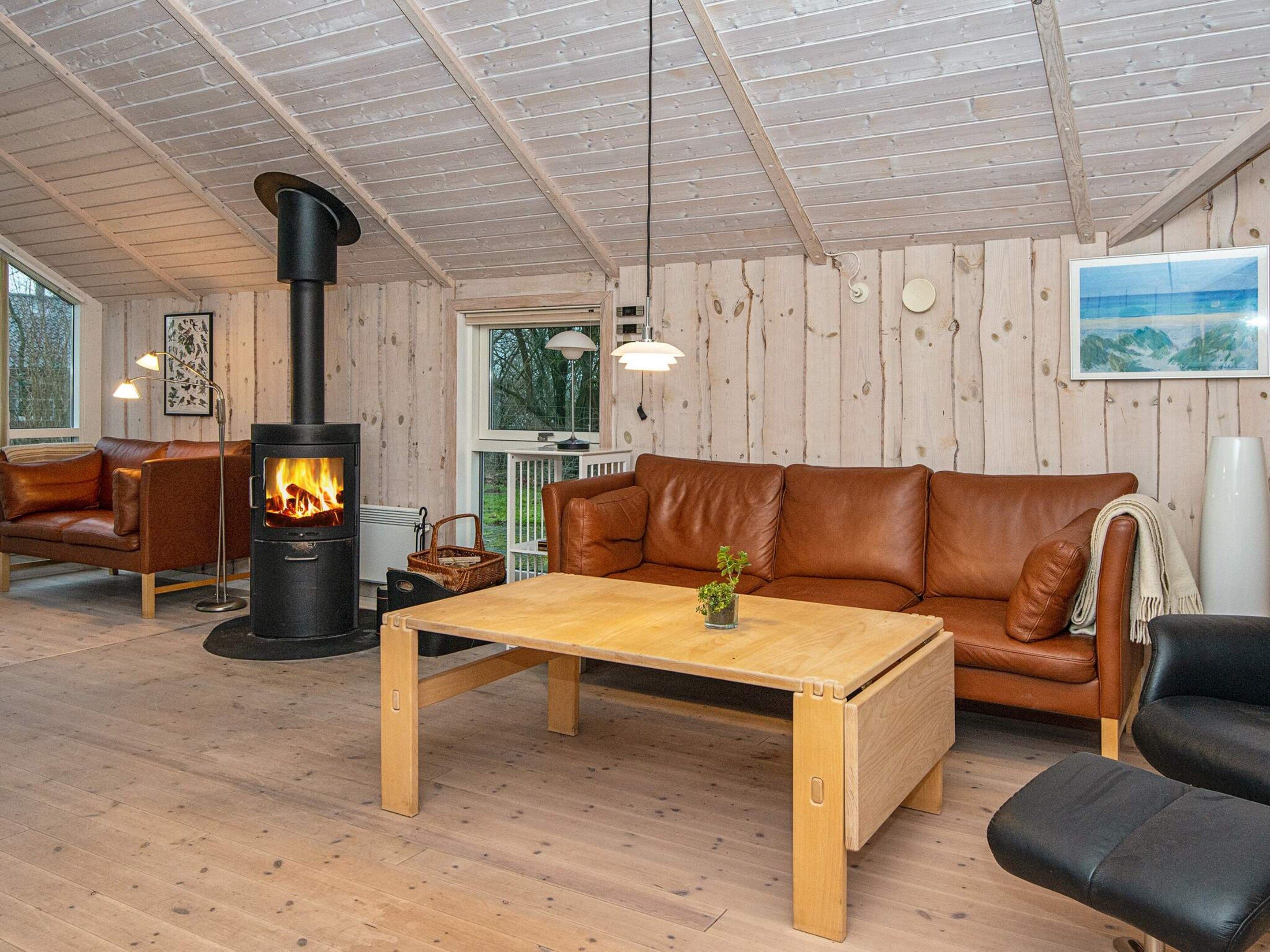 A cozy room with a fireplace, leather sofa, wooden table, and a view of the outdoors.