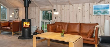 A cozy room with a fireplace, leather sofa, wooden table, and a view of the outdoors.