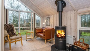 Et hyggeligt rum med et stort vindue, en lædersofa, en træstol og en brændeovn.