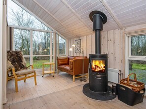 Una habitación acogedora con un ventanal grande, un sofá de cuero, una silla de madera y una estufa de leña.