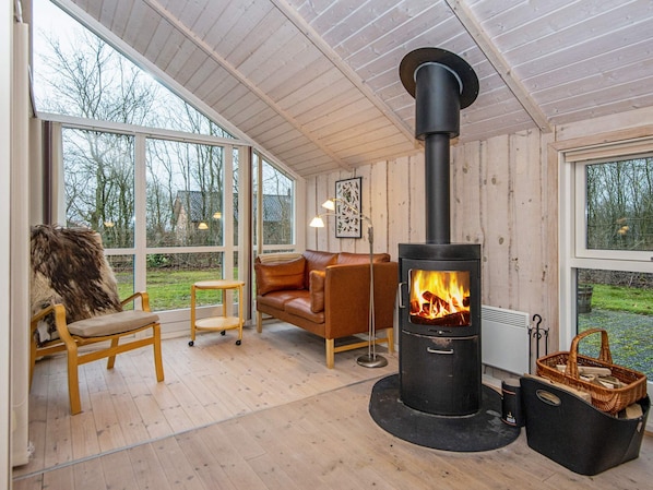 A cozy room with a large window, a sofa, a table, and a wood-burning stove. - 7 Person Holiday Home in Toftlund-by Traum (Toftlund)