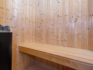 A wooden sauna with a bench and a stone wall.