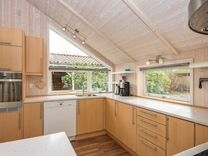 A modern kitchen with wooden cabinets, a built-in dishwasher, a coffee machine, and large windows providing natural light. - 7 Person Holiday Home in Toftlund-by Traum (Toftlund)