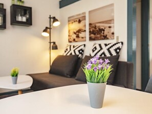 Moderni sisustus, jossa on harmaa pöytä, harmaa maljakko violetteja kukkia, harmaa sohva sekä mustavalkoisia kuvioilla varustettuja koristetyynyjä.