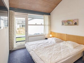 A hotel room with a bed, a window with curtains, a radiator, a nightstand with a lamp, and a wall decoration. - 4 Person Holiday Home in Vaeggerlose (Vaeggerlose)