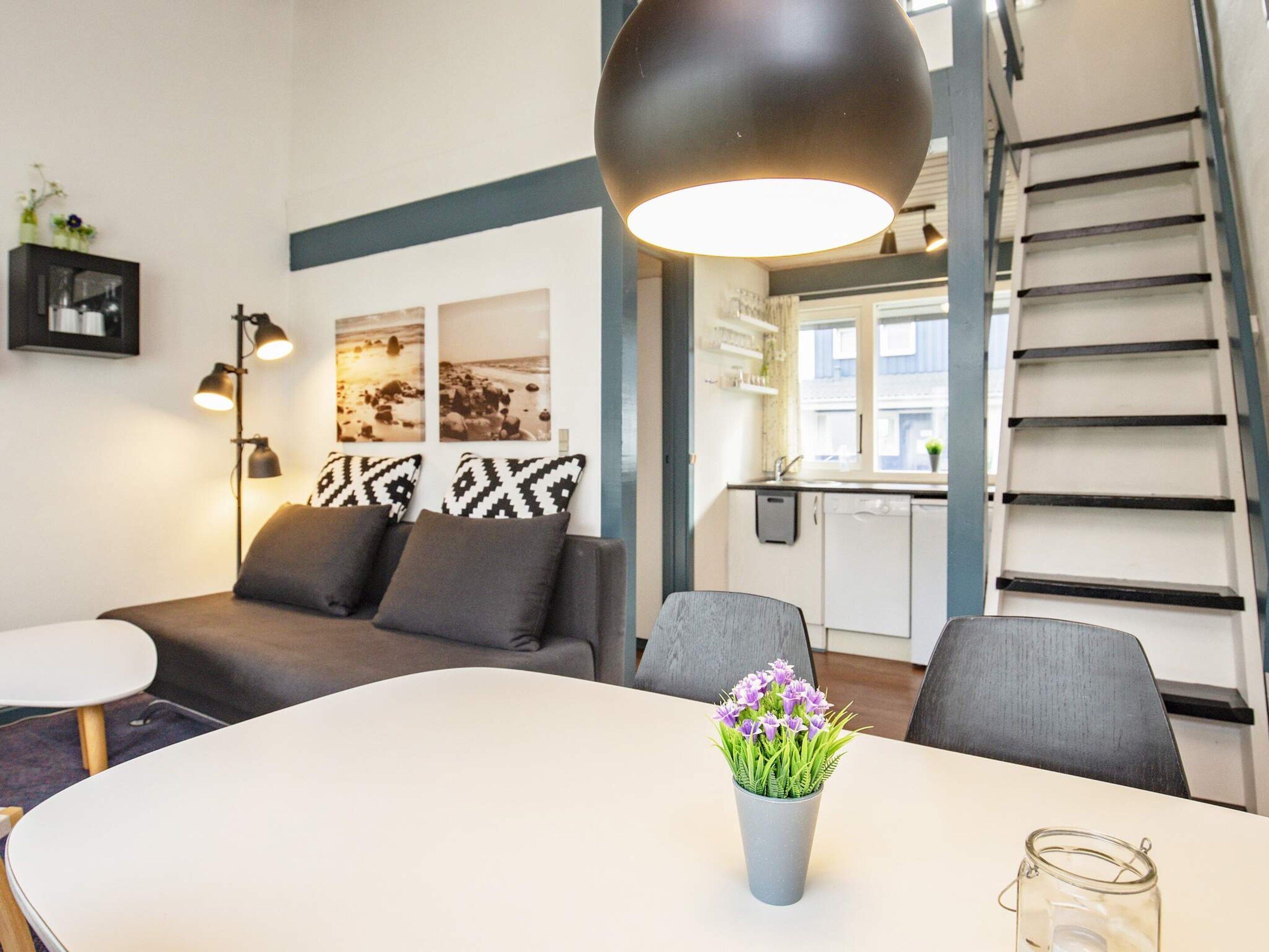 A modern living room with a sofa, a dining table with a vase of flowers, and a kitchen in the background.