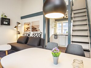 A modern living room with a sofa, a dining table with a vase of flowers, and a kitchen in the background. - 4 Person Holiday Home in Vaeggerlose (Vaeggerlose)
