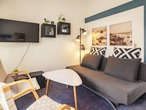 Una sala de estar moderna con un sofá, una mesita, una silla y una lámpara. Hay estantes en la pared con adornos.