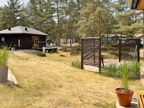 En stuga av trä med en veranda och utomhusmöbler, omgiven av en gräsyta och träd.