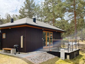 En modern stuga med en veranda, en grill och en stenlagd gångväg som leder till entrén.