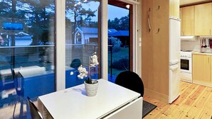 Une cuisine moderne avec un plan de travail blanc, une petite table ornée d’une orchidée en pot et une vue sur un quartier résidentiel, visible à travers de grandes fenêtres.