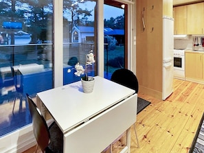 Une cuisine moderne avec un plan de travail blanc, une petite table ornée d’une orchidée en pot et une vue sur un quartier résidentiel, visible à travers de grandes fenêtres.