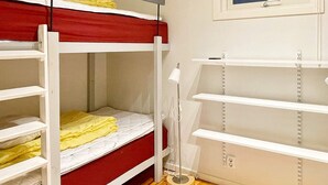 Un lit superposé avec un matelas rouge et du linge de lit blanc, une table de chevet avec une lampe et une fenêtre donnant sur un paysage bleu.