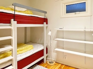 Un lit superposé avec un matelas rouge et du linge de lit blanc, une table de chevet avec une lampe et une fenêtre donnant sur un paysage bleu.