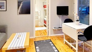 Un espace de vie compact comprenant un bureau, une chaise et un téléviseur. Une petite table recouverte d’une nappe à carreaux est placée au premier plan.