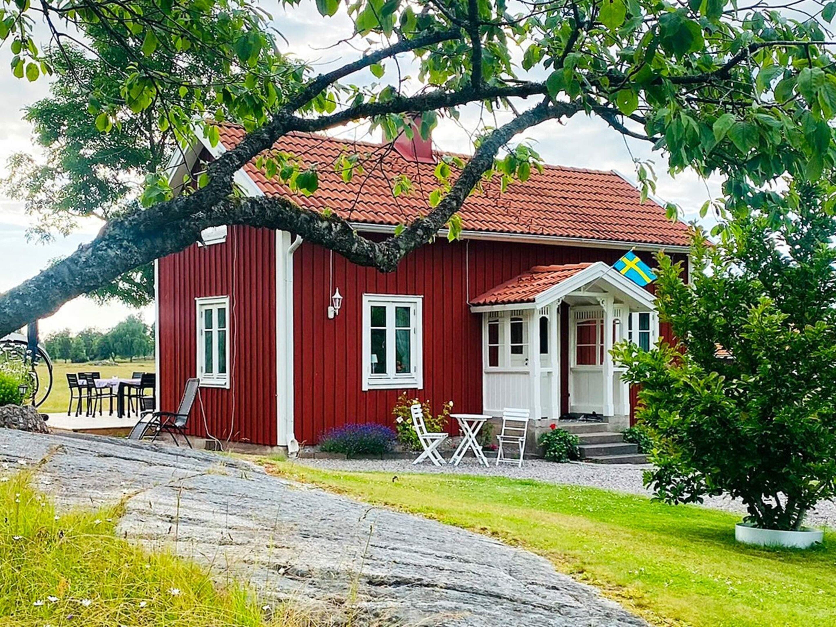 A red wooden house with a tiled roof, white windows, and a porch with outdoor seating.