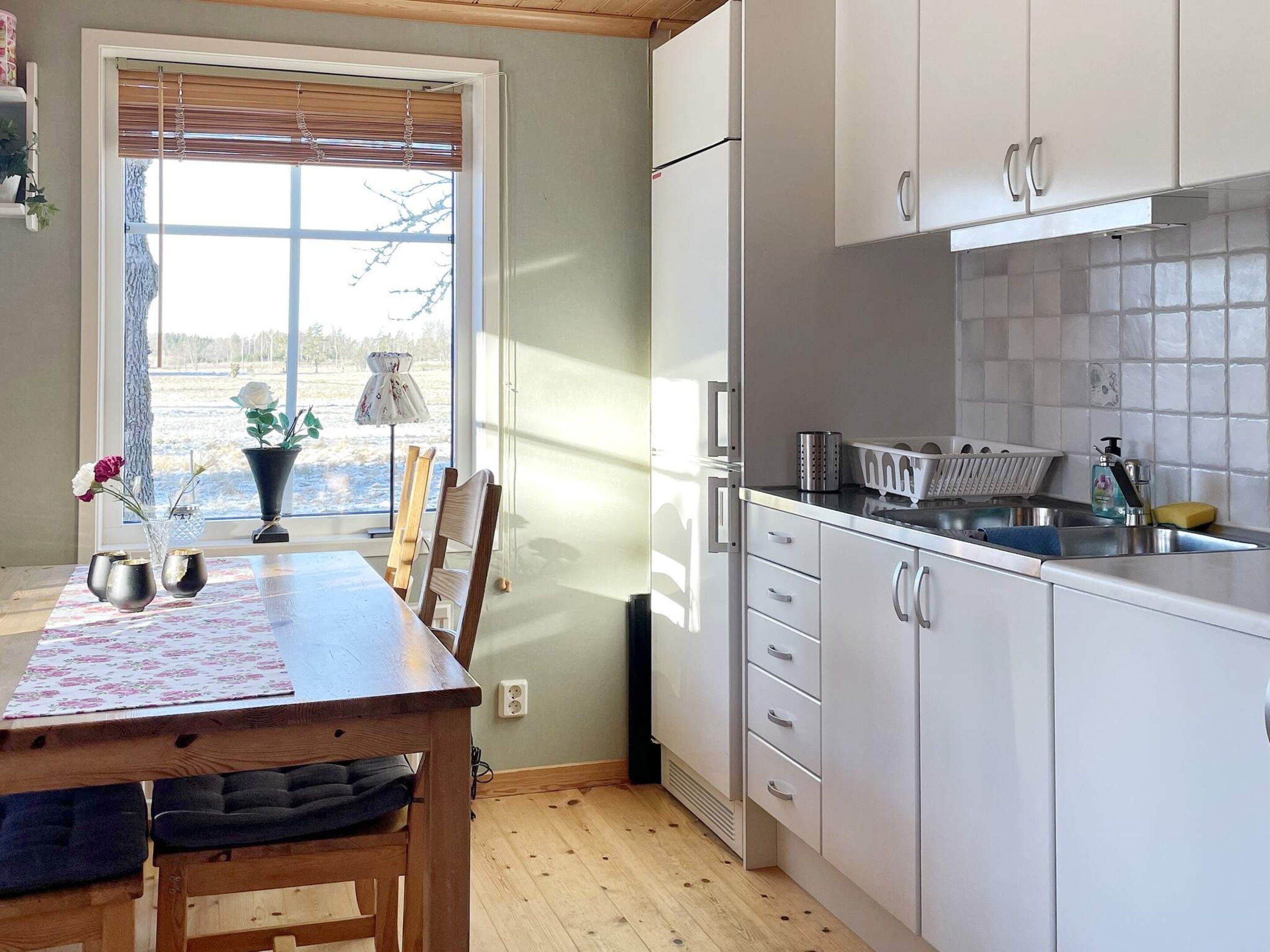 A kitchen with white cabinets, a wooden table, and a window with blinds.