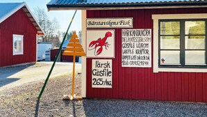 A red building with a corrugated metal roof, a signboard advertising seafood, and a contact number. - 6 Person Holiday Home in Lidkoping (Lidköping)