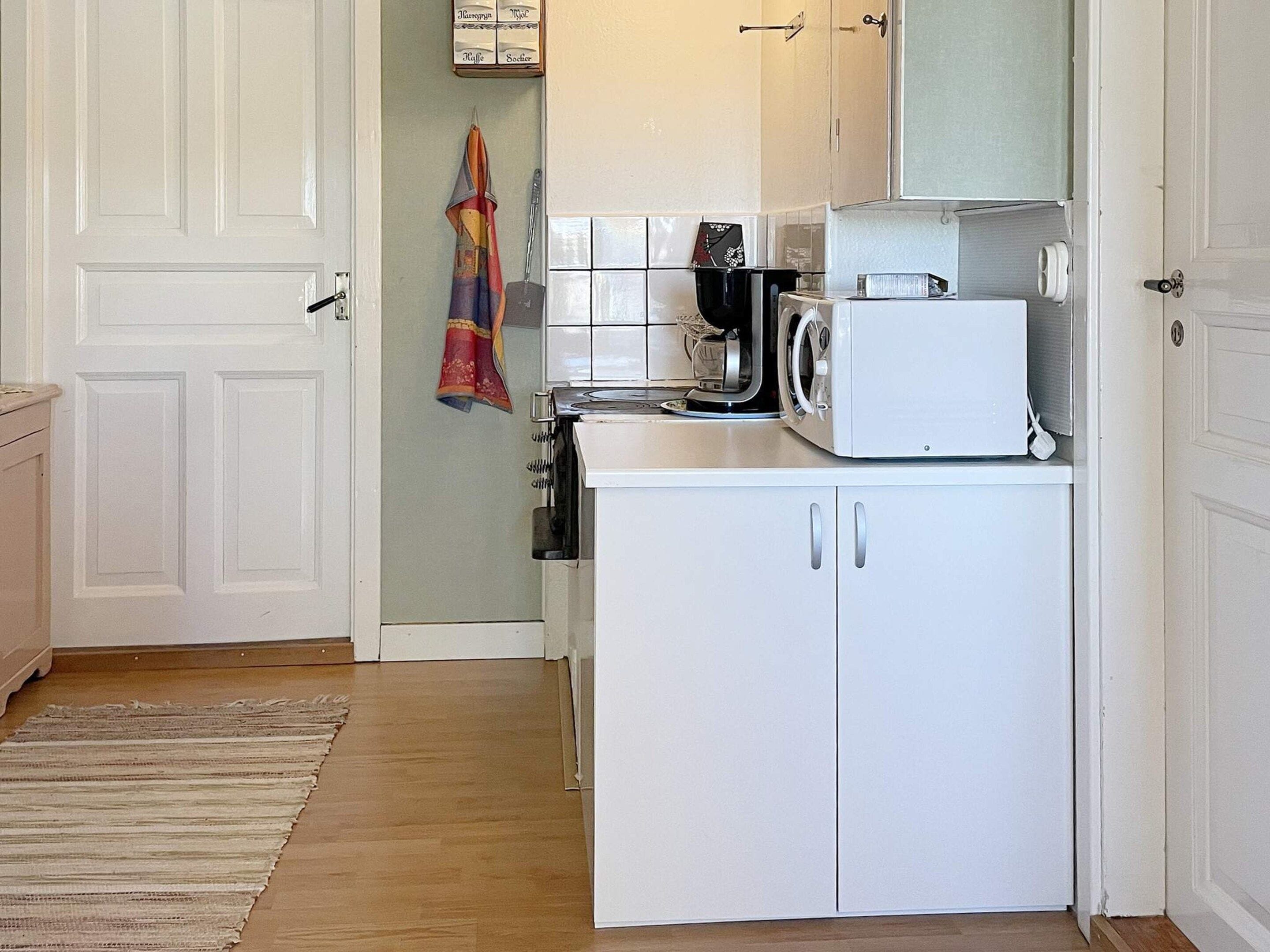 Una cocina compacta con armarios blancos, un microondas y una tetera.