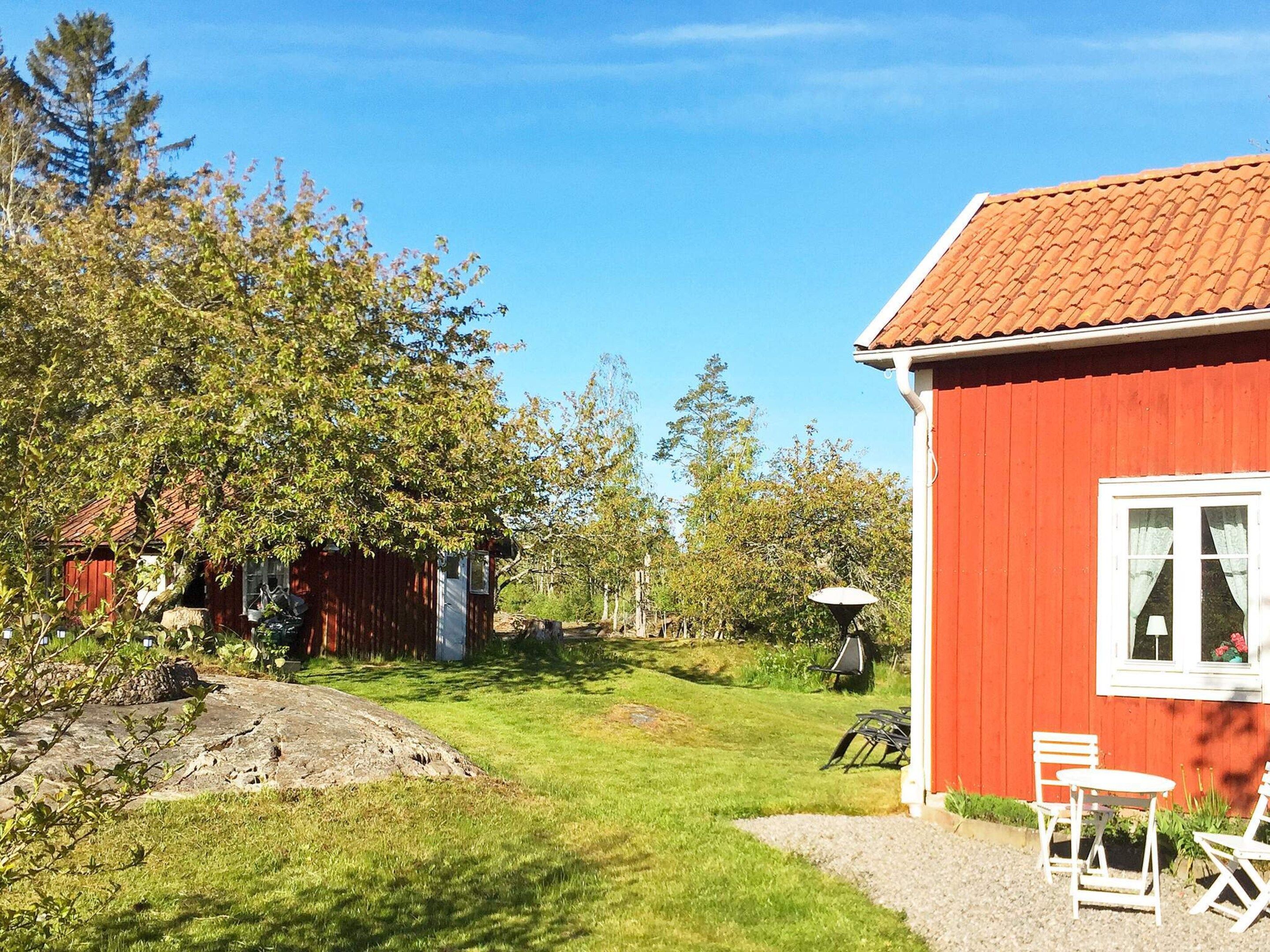 Una casa de madera roja con techo de tejas, un pequeño jardín con césped y un conjunto de mesa y silla blancos en el exterior.