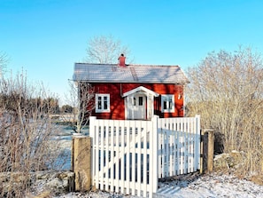 A red house with a white door and windows, surrounded by a white fence. - 6 Person Holiday Home in Lidkoping (Lidköping)