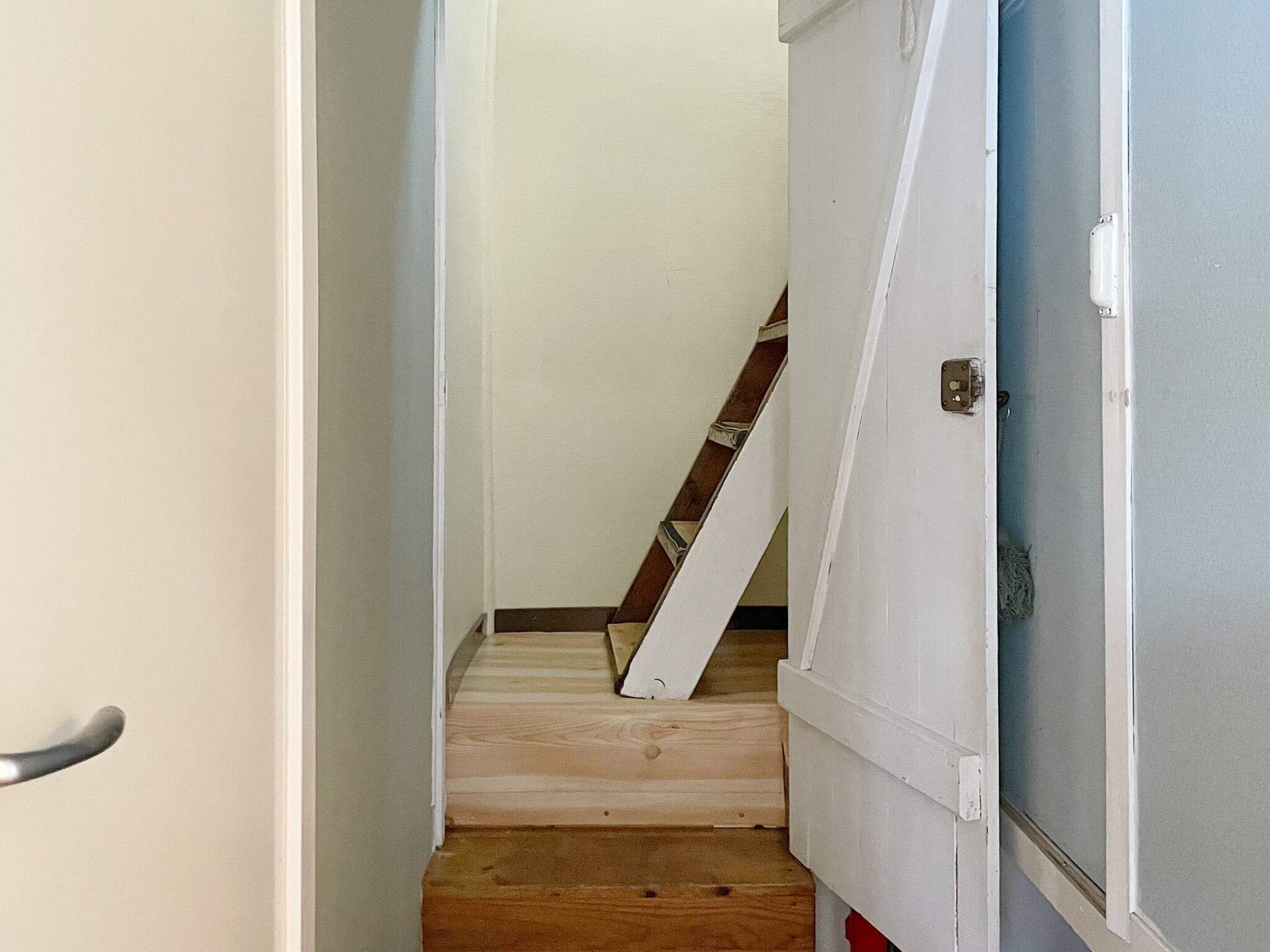 Un pasillo estrecho con una escalera de madera que lleva a una puerta con pomo metálico.