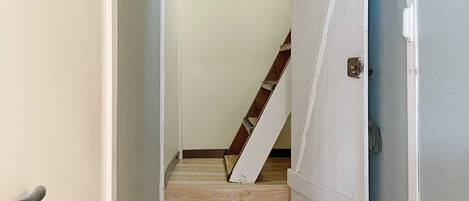 A narrow hallway with a wooden staircase leading to a door with a metal handle.