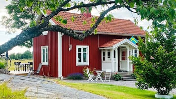 A red wooden house with a tiled roof, white windows, and a porch with outdoor seating.