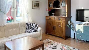 Una sala de estar con un sofá, un aparador de madera, un televisor y un tapete floral.