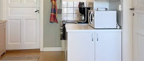 A compact kitchen with white cabinets, a microwave, and a kettle.