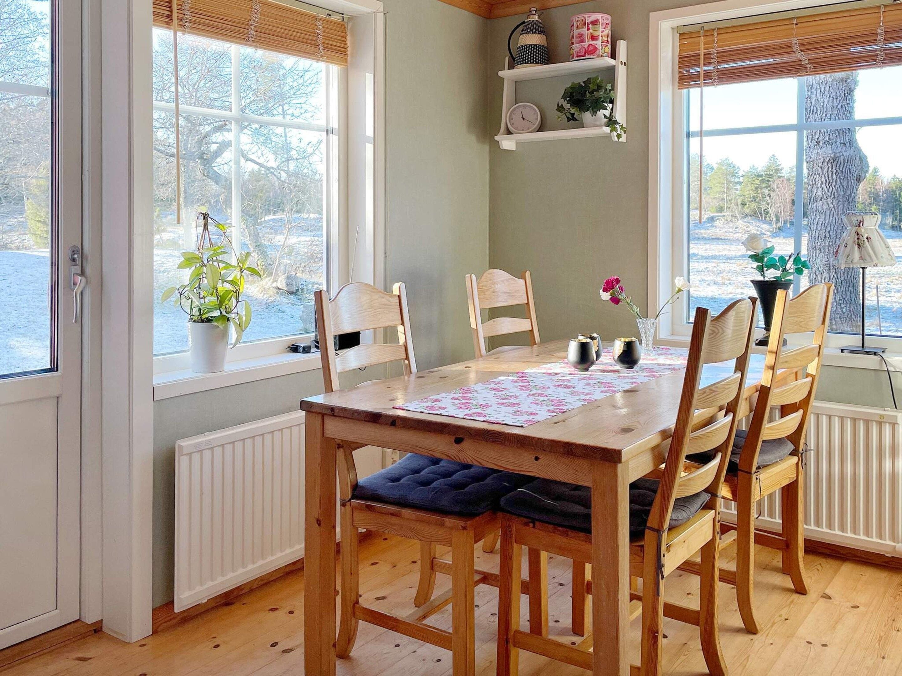 Un comedor con mesa y sillas de madera, una ventana que ofrece vistas a árboles, y un estante con objetos decorativos.