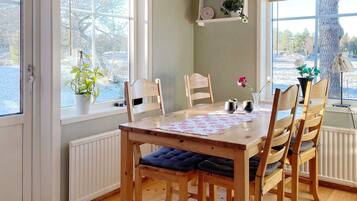 A dining area with a wooden table and chairs, a radiator, and a window with a view of trees.
