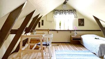 A small, cozy attic bedroom with a sloped ceiling, a single bed, a chair, a small table, and a window with curtains.