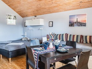 A cozy room with a wooden ceiling, a dining table with chairs, a sofa with striped cushions, and a framed picture on the wall. - 4 Person Holiday Home in Lottorp (Byxelkrok)