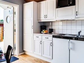 Een moderne keuken met witte kastjes, een zwart fornuis en een schaal fruit op het aanrecht.