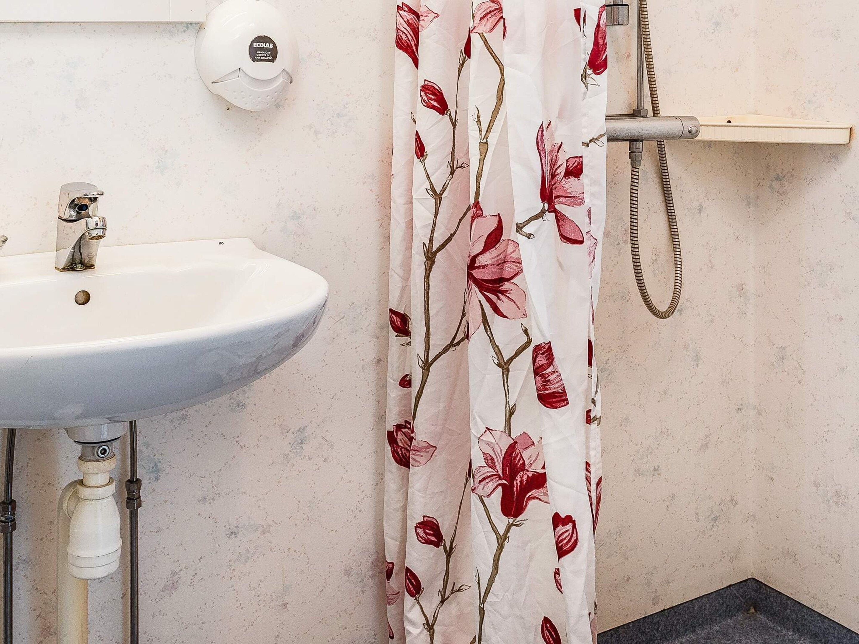 Un baño con un lavamanos blanco, dispensador de jabón para manos y cortina de ducha con estampado floral.