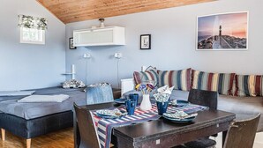 A cozy living room with a wooden ceiling, a sofa set, a dining table with chairs, and a large window. - 4 Person Holiday Home in Lottorp (Byxelkrok)