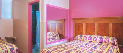 A bedroom with a pink and beige color scheme, a wooden headboard, a large mirror, and a patterned bedspread.