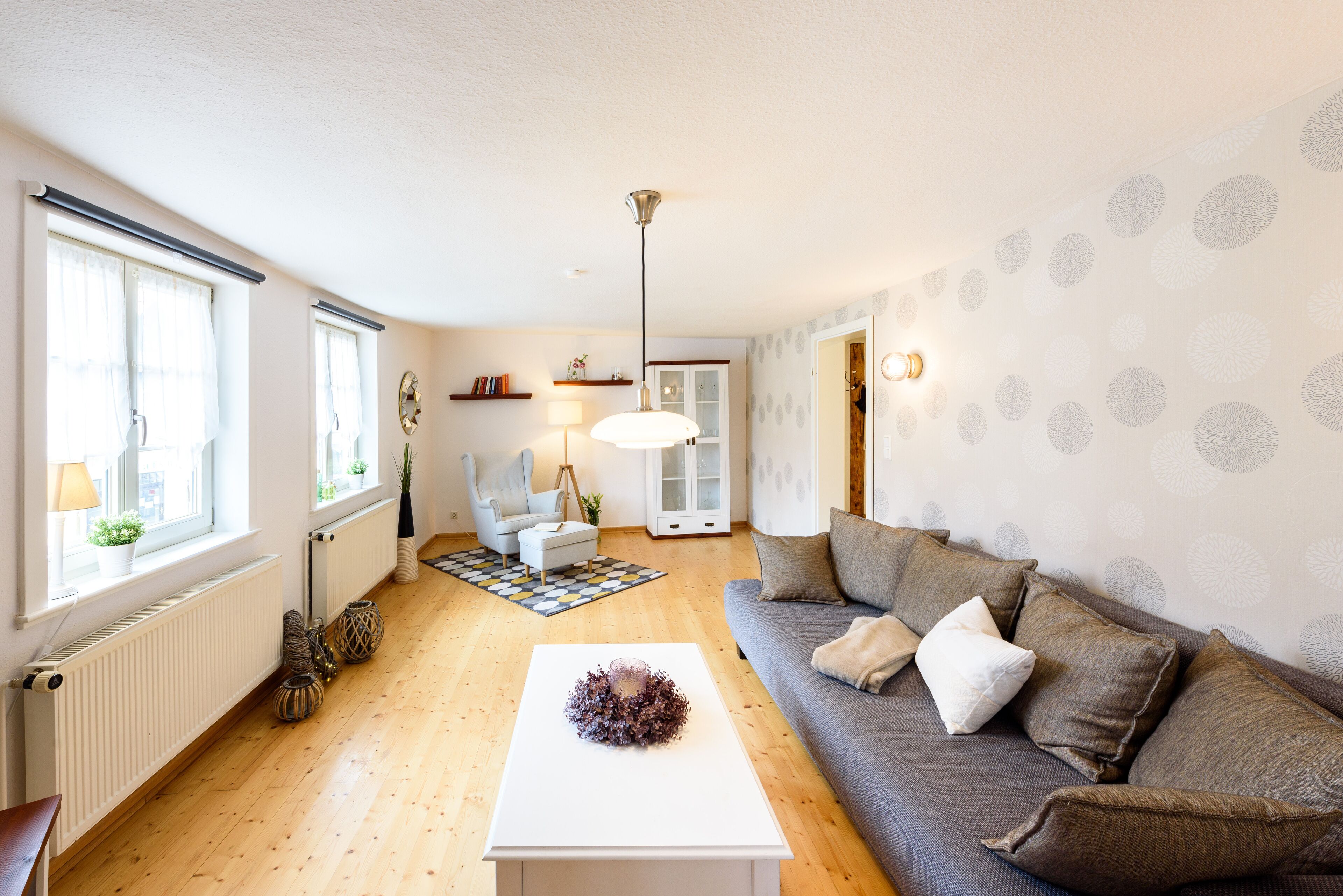 Ein modernes Wohnzimmer mit einer Couch, einem Couchtisch und einer Lampe. Ein Fenster mit Vorhängen und eine Heizung sind an der Wand angebracht.