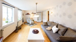 A modern living room with a sofa, a coffee table, and a lamp. There is a window with curtains and a radiator on the wall. - Ackerbürgerhof Ballstraße 18 (Quedlinburg)